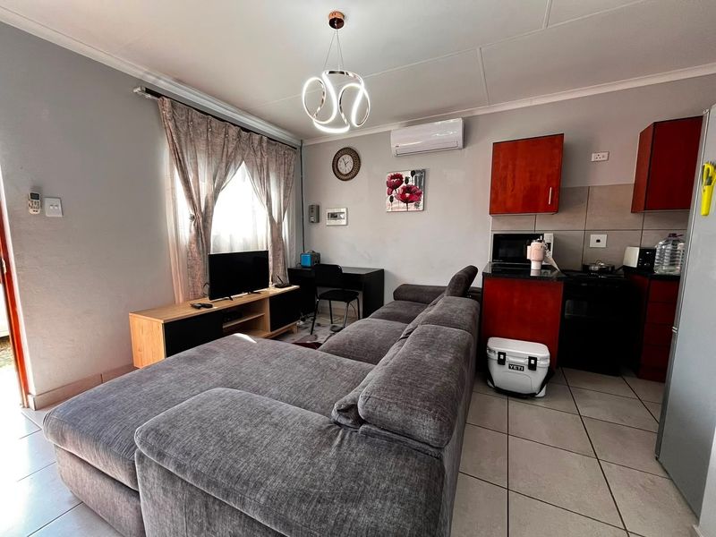 Open-plan living area featuring tiled floors, a split-system air conditioner, and a compact kitchen with built-in cabinetry and granite countertops.