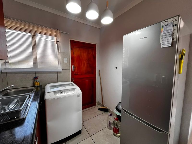 A functional laundry room featuring tiled flooring, a stainless steel sink, and direct access to an exterior door.