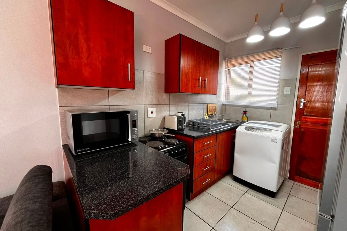 Compact kitchen featuring dark wood cabinetry, granite countertops, tiled backsplash, and integrated laundry plumbing, providing a functional and efficient workspace.