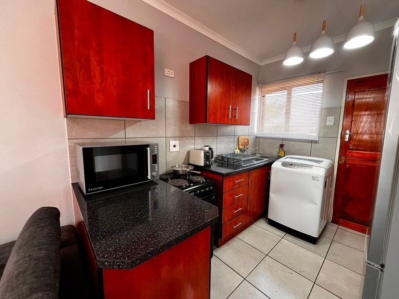 Compact kitchen featuring dark wood cabinetry, granite countertops, tiled backsplash, and integrated laundry plumbing, providing a functional and efficient workspace.