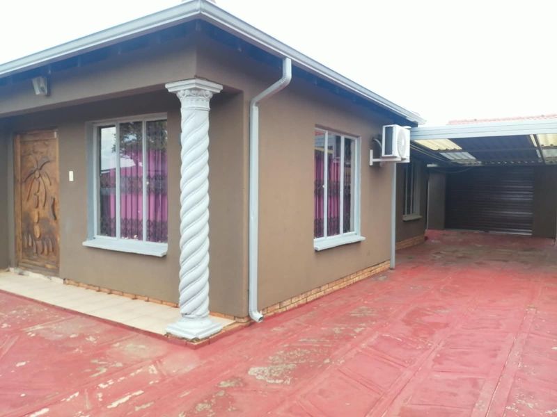 Front exterior view of the house featuring a decorative column, paved driveway, and an attached carport area.