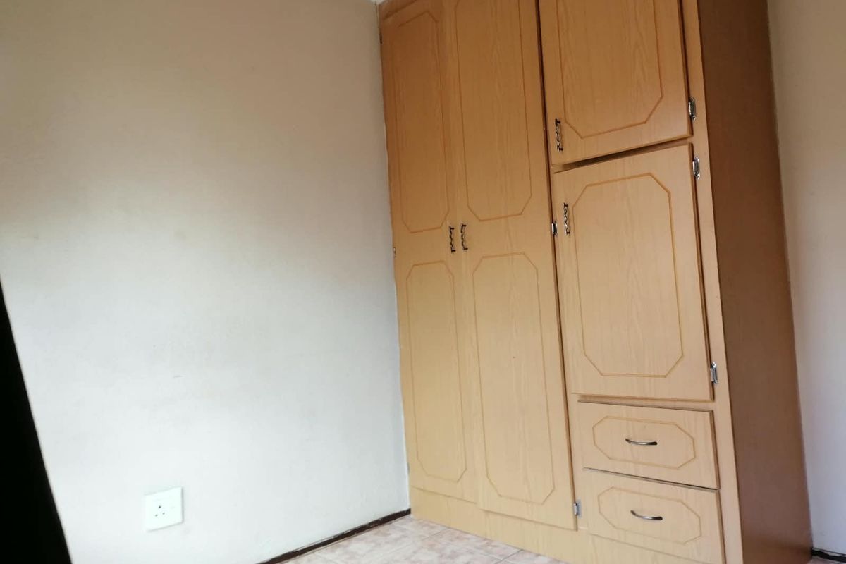A bedroom featuring a built-in wooden wardrobe, tiled flooring, and decorative coving, offering a functional space ready for personalization.