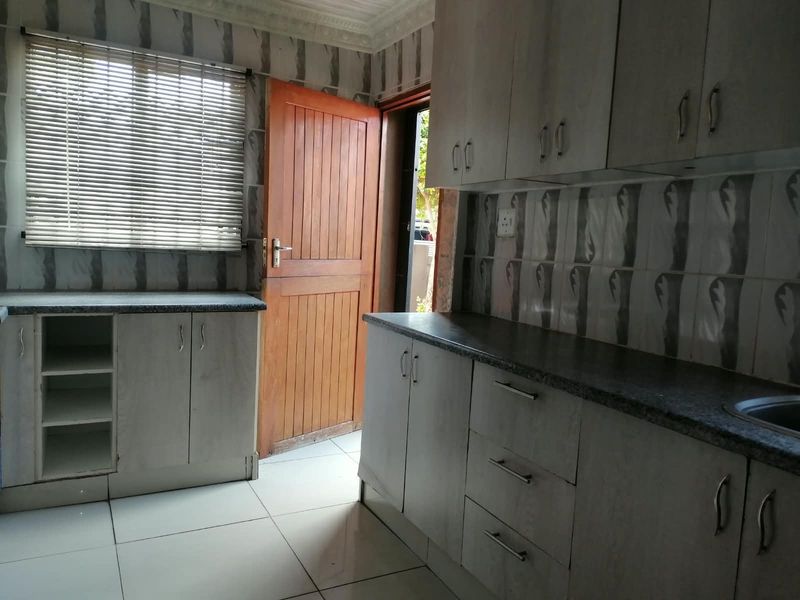 A functional kitchen featuring built-in cabinetry, laminate countertops, a stainless steel sink, and tiled flooring with direct access to the exterior.