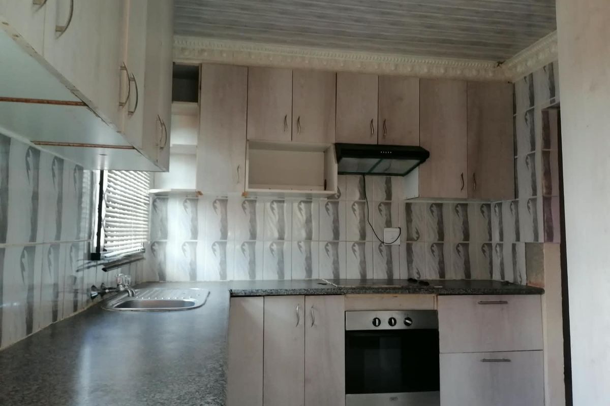 A functional kitchen featuring built-in cabinetry, a stainless steel sink, an integrated oven, and an extractor fan, ready for a modern update.