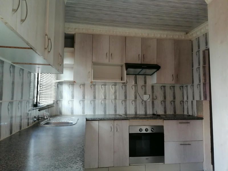 A functional kitchen featuring built-in cabinetry, a stainless steel sink, an integrated oven, and an extractor fan, ready for a modern update.