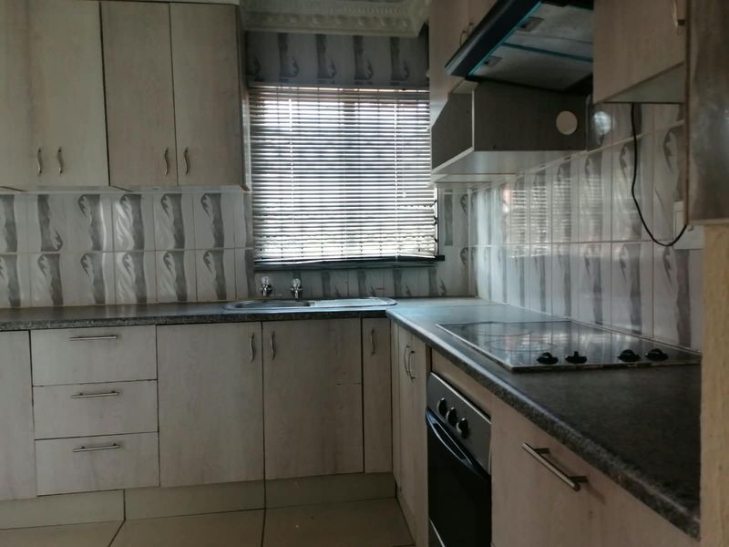A functional kitchen featuring built-in cabinetry, laminate countertops, a stainless steel sink, and integrated cooking appliances including an oven and electric hob.