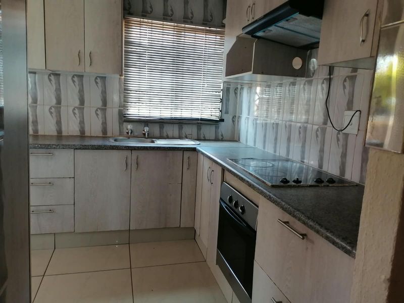 Functional kitchen featuring built-in cabinetry, laminate countertops, integrated oven, hob, and extractor fan with tiled backsplash and flooring.