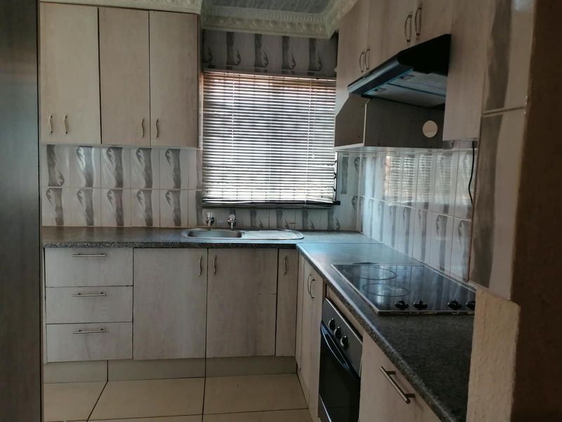 A functional kitchen featuring built-in cabinetry, granite countertops, a stainless steel sink, and integrated appliances including an electric hob, oven, and extractor fan.