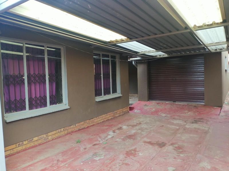 Front exterior view featuring a covered carport, roller shutter garage door, and paved driveway with security-fitted windows.