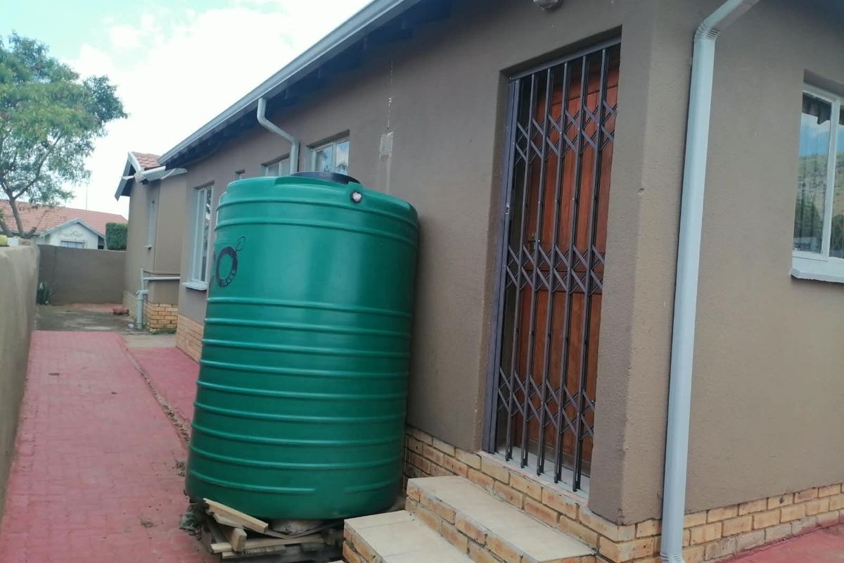 Rear exterior view of the house featuring a water storage tank, security gate, and paved walkway.