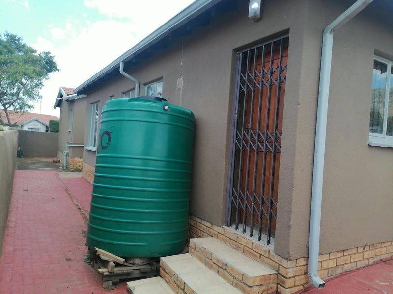Rear exterior view of the house featuring a water storage tank, security gate, and paved walkway.