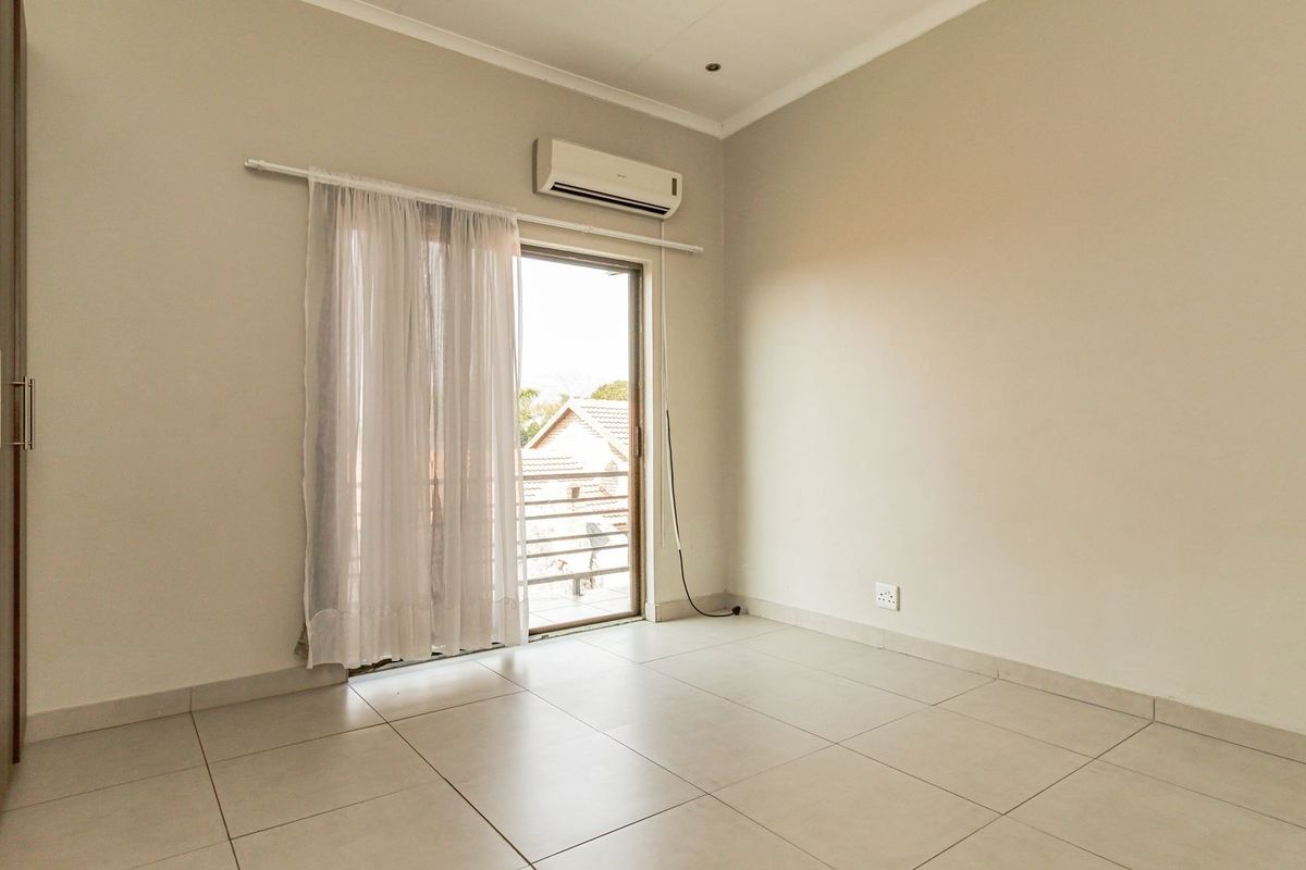 A bright, empty bedroom featuring tiled flooring, built-in cupboards, an air conditioning unit, and a sliding glass door leading to an outdoor area.
