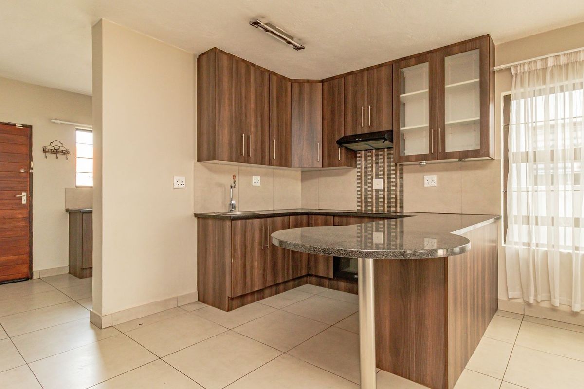 A functional kitchen featuring wood-look laminate cabinetry, granite countertops with an integrated breakfast bar, and neutral tiled flooring.