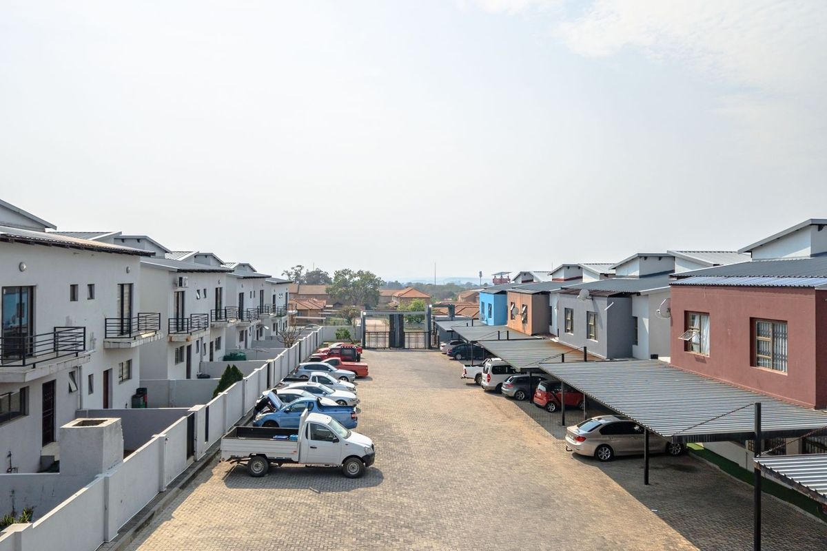 Aerial view of a townhouse complex featuring paved driveway, covered parking bays, and perimeter security walls.