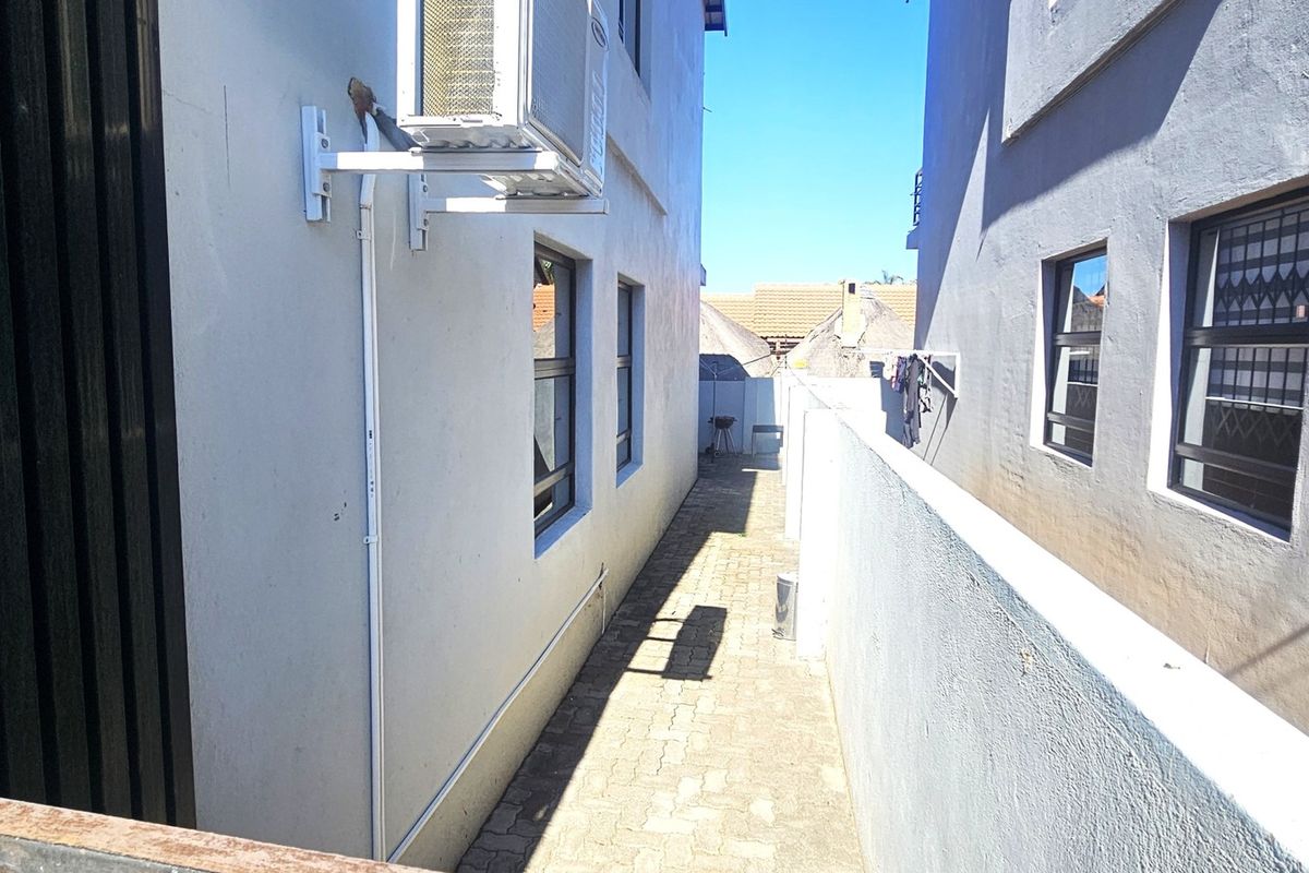 A narrow side passage between two townhouse structures featuring paved flooring, boundary walls, and an externally mounted air conditioning unit.