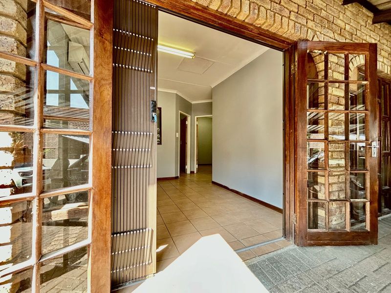Entrance area featuring tiled flooring, exposed brick accents, and timber-framed glass doors leading into the interior hallway.