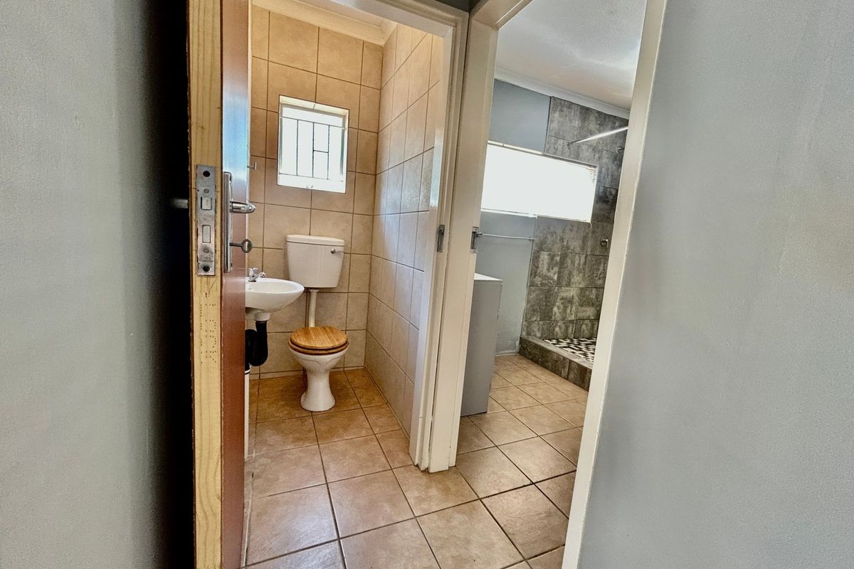 A functional bathroom featuring tiled flooring and walls, a pedestal basin, toilet, and a separate shower enclosure with a tiled finish.