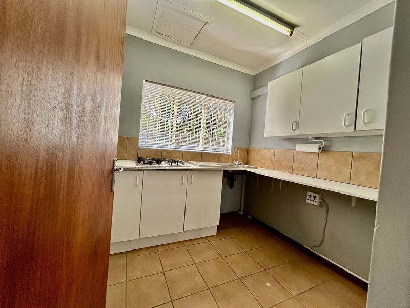 A functional kitchen featuring built-in cabinetry, a gas hob, stainless steel sink, and tiled splashbacks, offering a clean and practical workspace.