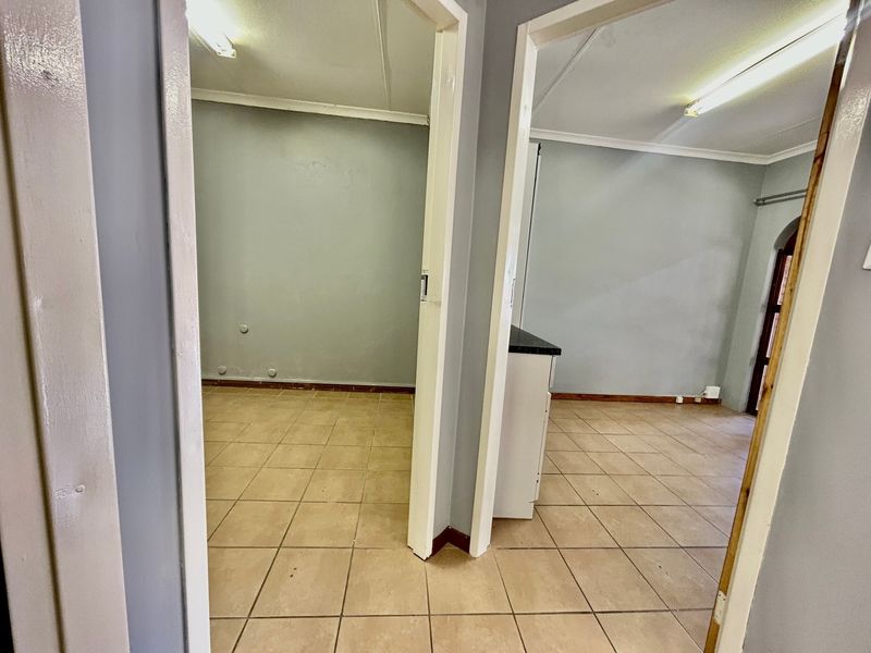 A view from a hallway looking into two empty rooms featuring tiled flooring and basic fluorescent lighting.