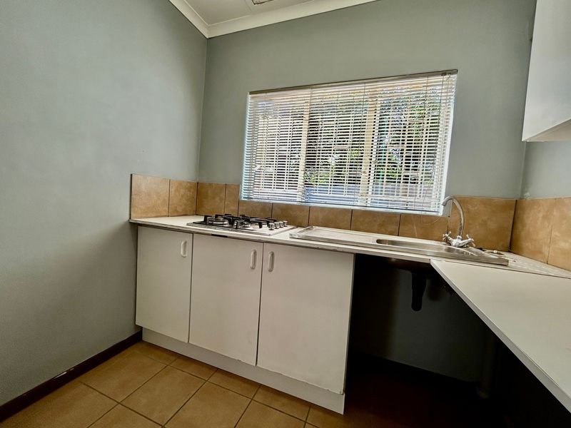 A functional kitchen area featuring a gas hob, stainless steel sink, tiled splashback, and built-in cabinetry with neutral wall finishes.