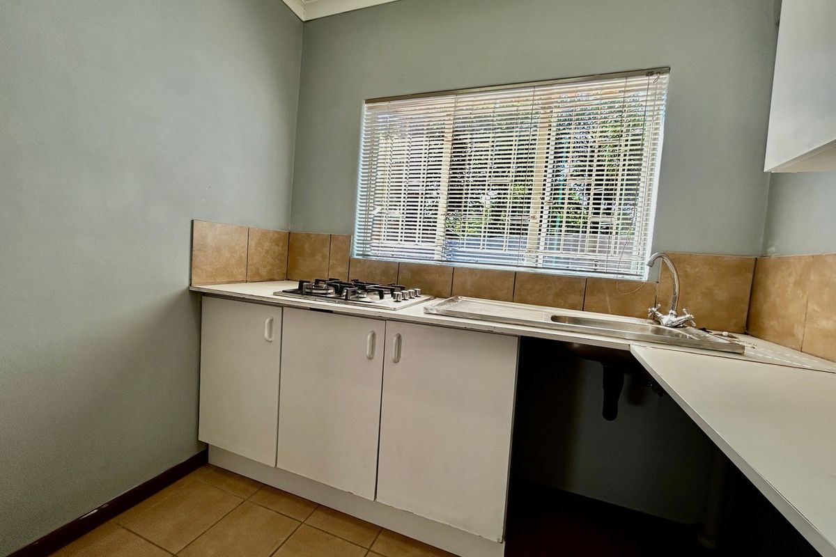 A functional kitchen area featuring a gas hob, stainless steel sink, tiled splashback, and built-in cabinetry with neutral wall finishes.