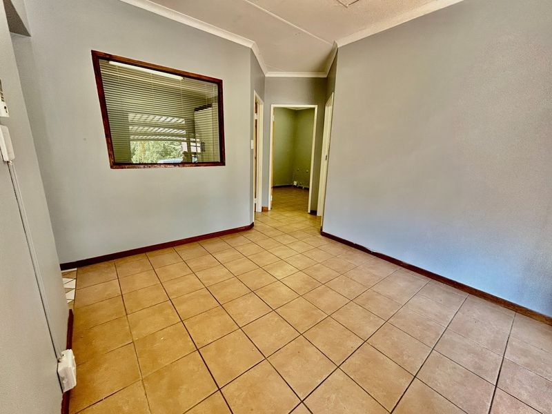 An empty hallway featuring tiled flooring, coved ceilings, and an internal window with a wooden frame, leading to adjacent rooms.