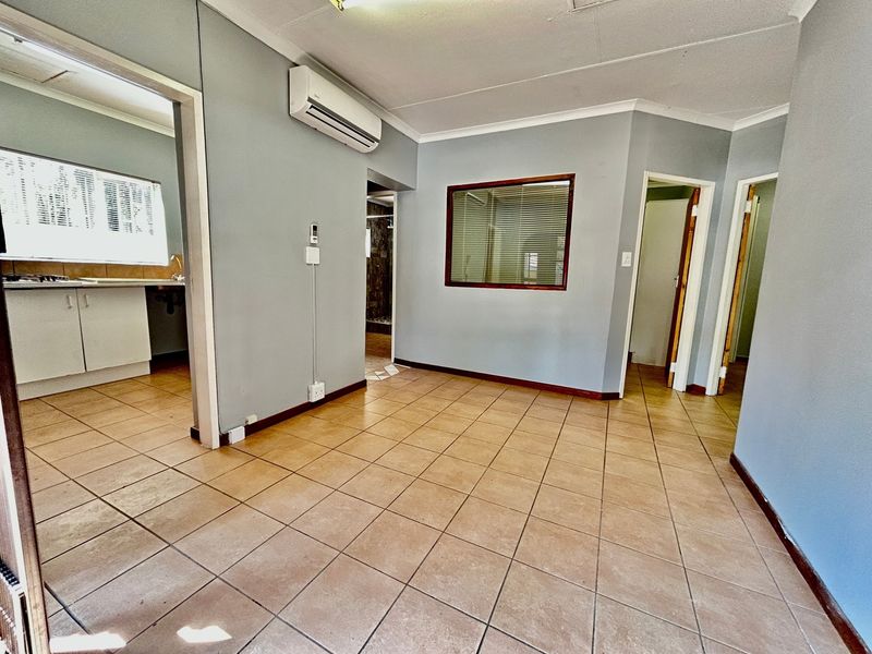 An open-plan living area featuring tiled flooring, a wall-mounted air conditioning unit, and an internal window, providing a neutral base for interior design.