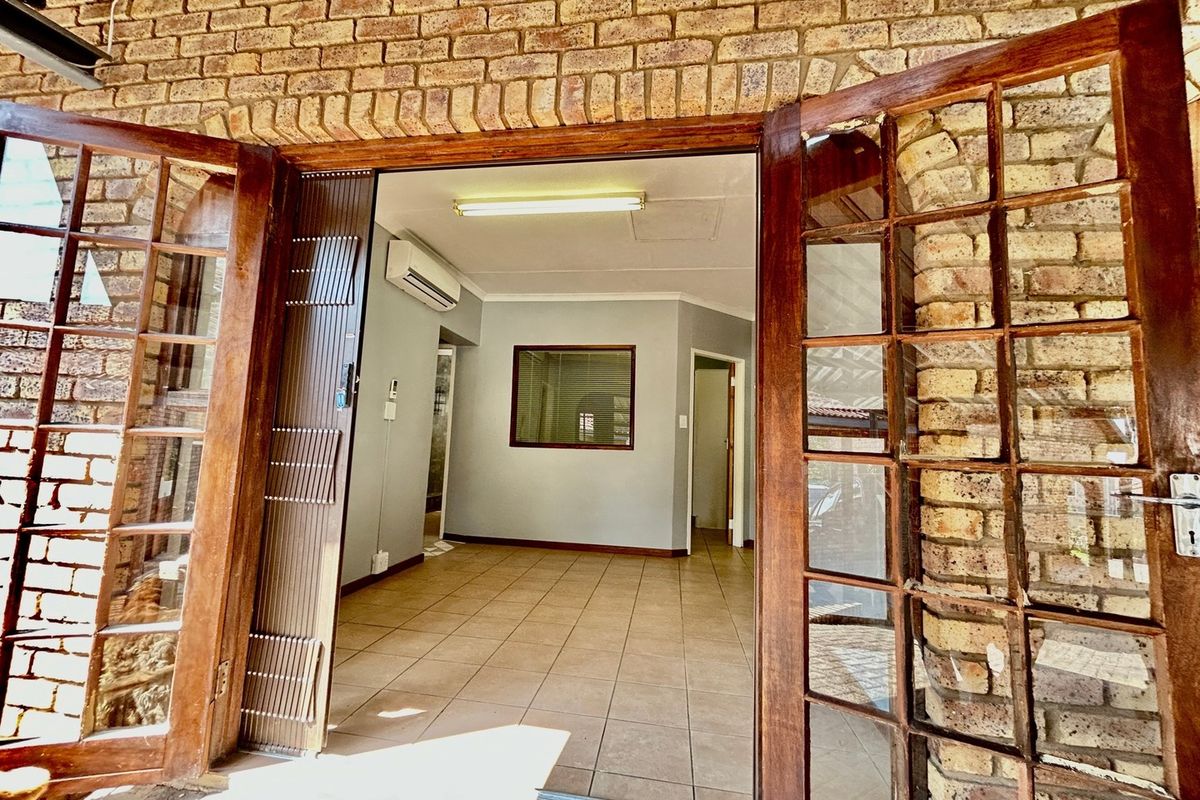 An empty living area featuring tiled floors, an air conditioning unit, and classic wooden french doors opening onto an exposed brick exterior.