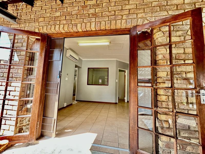 An empty living area featuring tiled floors, an air conditioning unit, and classic wooden french doors opening onto an exposed brick exterior.