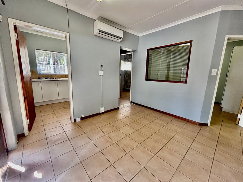 An empty living area featuring tiled flooring, a wall-mounted air conditioning unit, and an internal window looking through to an adjacent space.