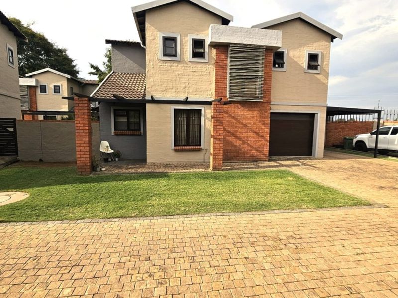 A double-story residential property featuring a brick-paved driveway, a single garage, and a well-maintained front lawn with brick pillar accents.