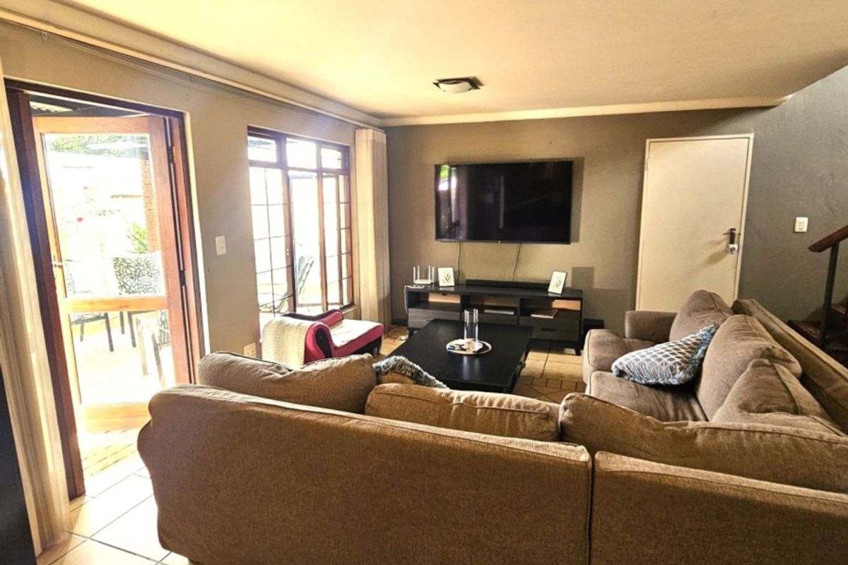 A comfortable living room featuring tiled flooring, large windows, and a sliding glass door providing direct access to the outdoor patio area.