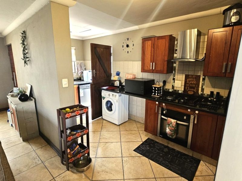 A functional kitchen featuring warm-toned wooden cabinetry, granite countertops, a built-in oven with gas hob, and tiled flooring throughout.