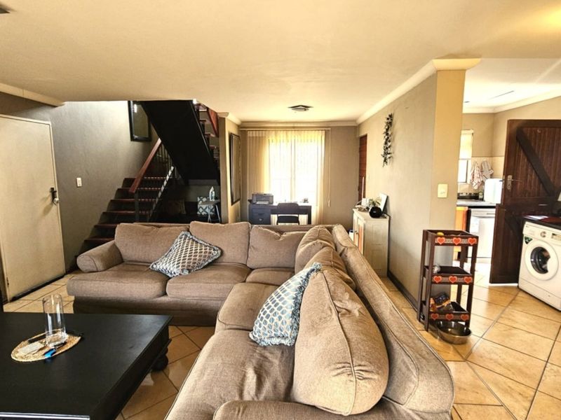 Open plan living area featuring tiled flooring and an integrated staircase, with a visible laundry area in the background.