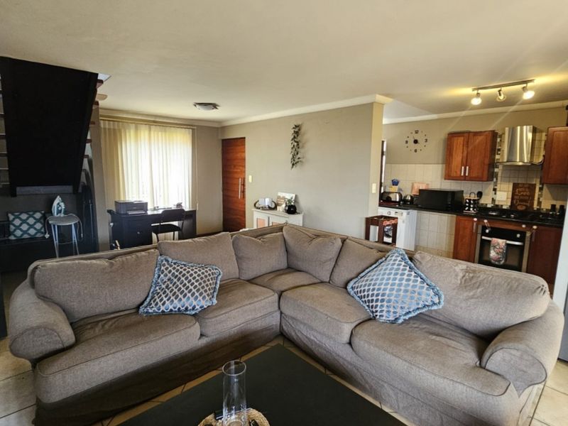 Open-plan living area featuring a functional kitchen with built-in cabinetry, oven, and cooktop, seamlessly connected to the main living space with tiled flooring.