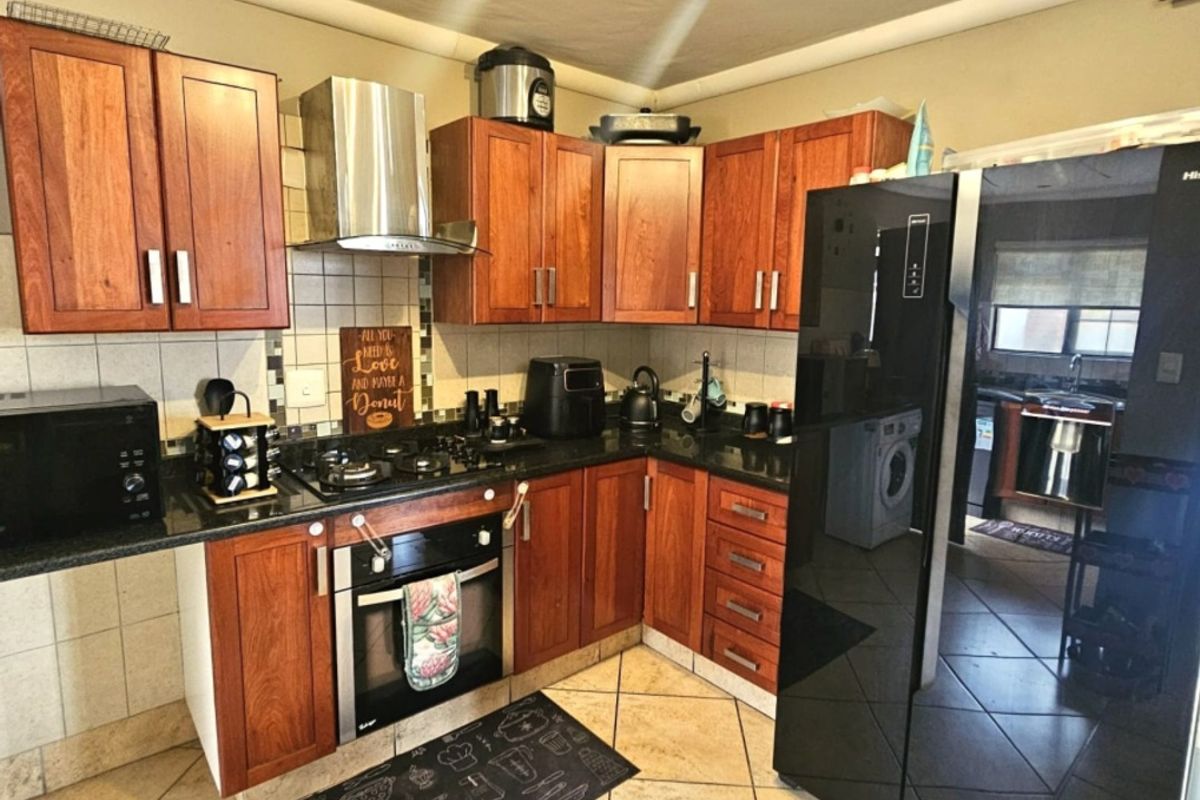 A functional kitchen featuring wooden cabinetry, granite countertops, a built-in oven with gas hob, and a stainless steel extractor fan, with tiled flooring throughout.
