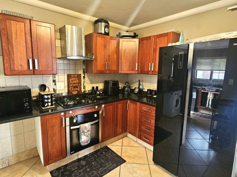 A functional kitchen featuring wooden cabinetry, granite countertops, a built-in oven with gas hob, and a stainless steel extractor fan, with tiled flooring throughout.