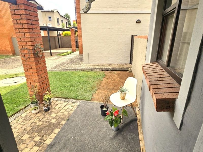 A small paved patio area featuring a brick pillar and window sill, overlooking a compact garden space.
