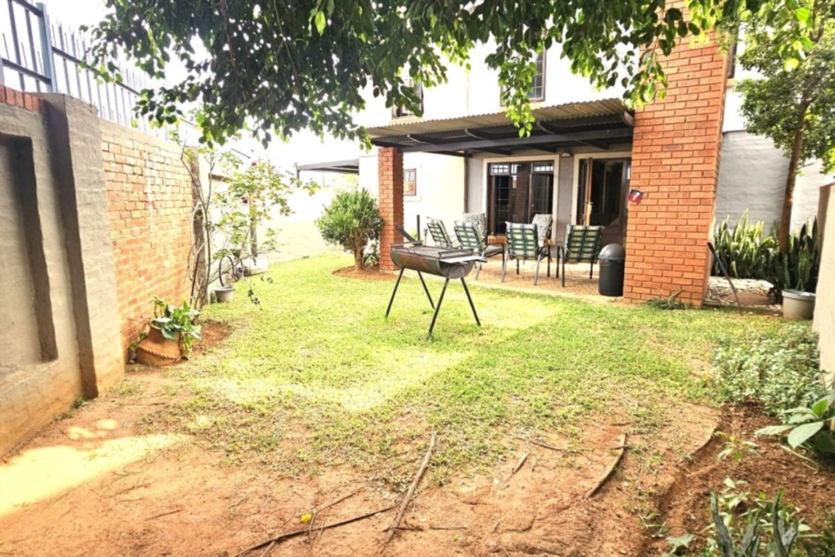 A rear garden view featuring a brick boundary wall, a covered patio area, and direct access to the home through sliding glass doors.