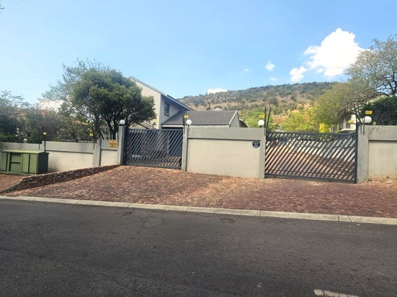Front view of the property featuring a paved driveway, secure metal gates, and a perimeter wall with exterior lighting.