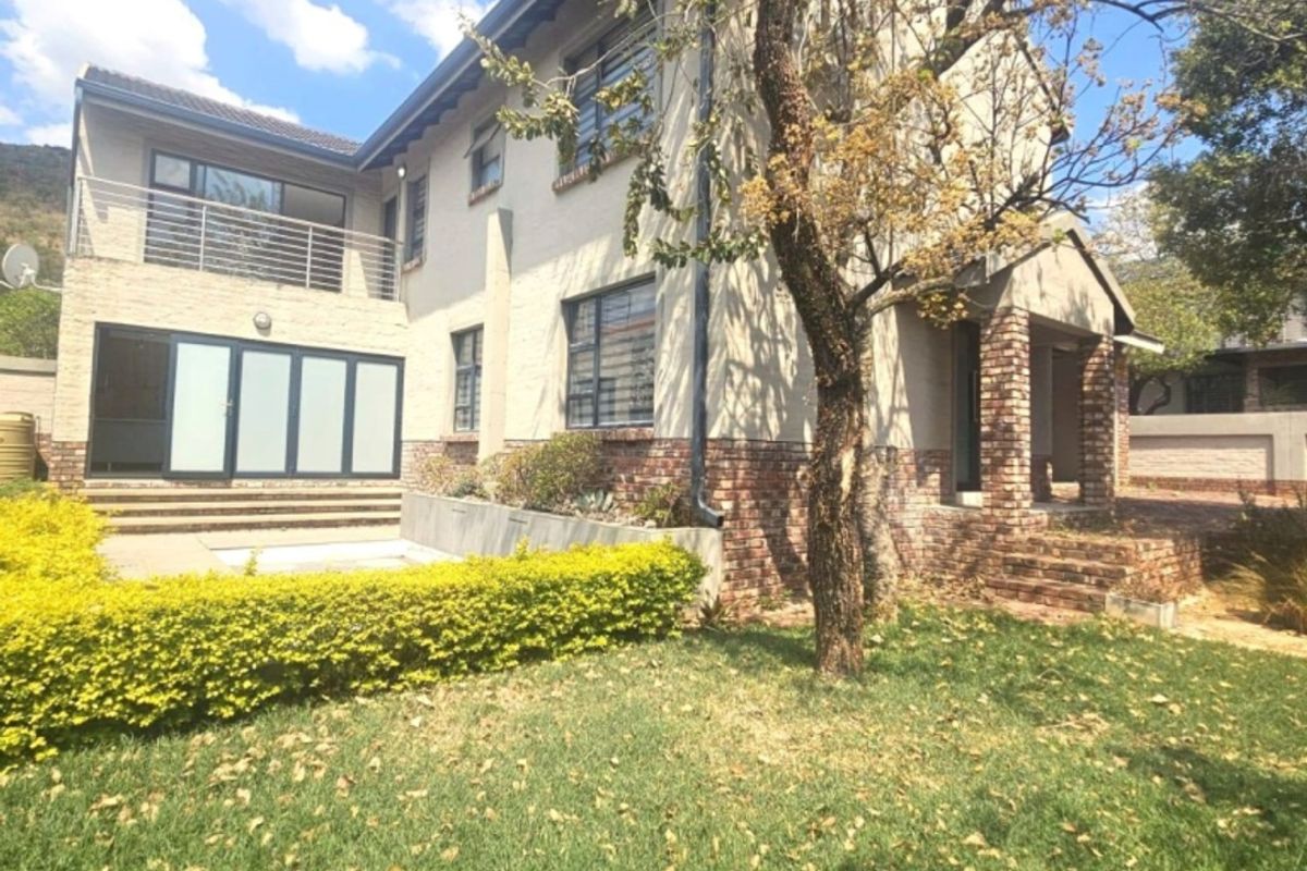 Rear view of a two-story brick house featuring a balcony, patio area, and established garden space.