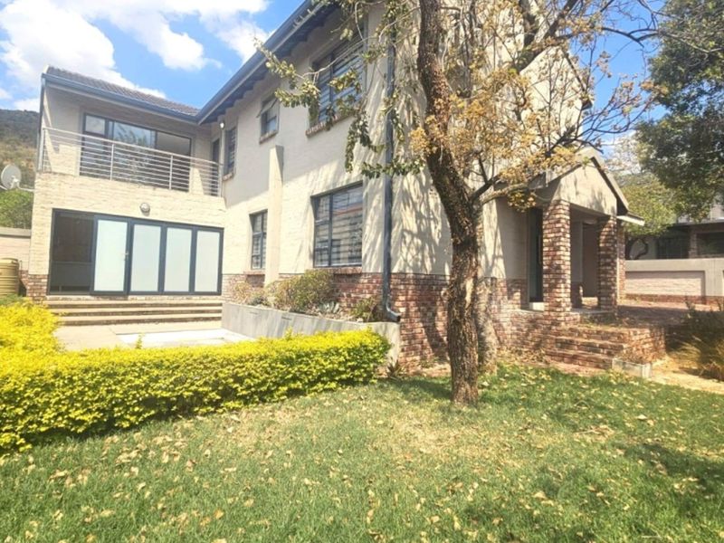 Rear view of a two-story brick house featuring a balcony, patio area, and established garden space.