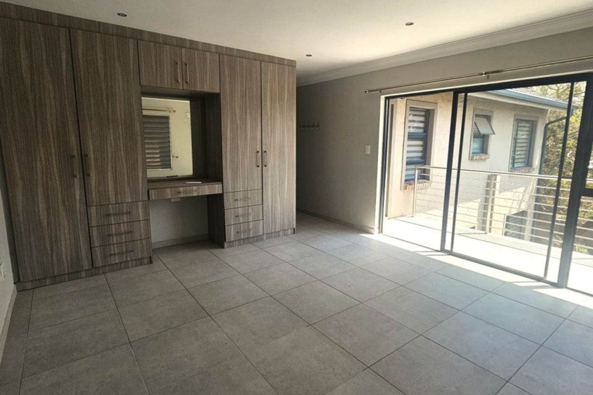 Spacious bedroom featuring modern tiled flooring, extensive built-in cabinetry with an integrated vanity, and large sliding glass doors leading to an outdoor balcony.