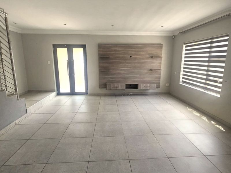 Spacious living room featuring large format floor tiles, recessed lighting, a built-in media console, and a modern staircase with a metal balustrade.