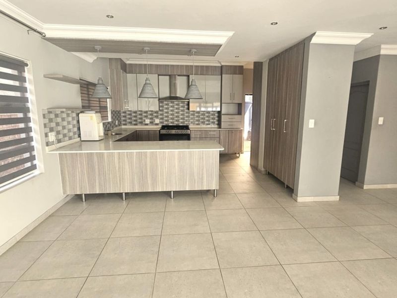 Modern open-plan kitchen featuring wood-grain cabinetry, stone countertops, a gas stove with extractor, and neutral tiled flooring throughout.