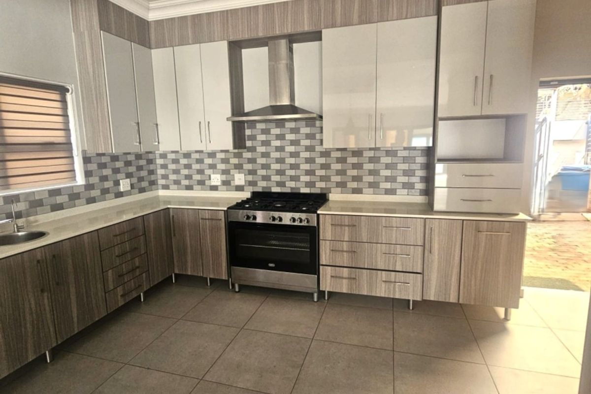 Modern kitchen featuring wood-grain and high-gloss cabinetry, stone countertops, a gas stove with extractor fan, and neutral tiled flooring.