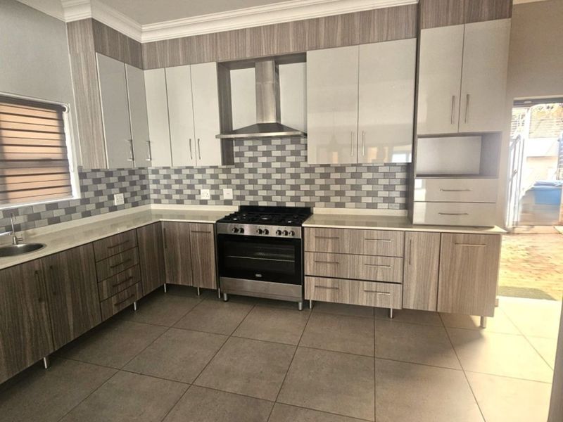 Modern kitchen featuring wood-grain and high-gloss cabinetry, stone countertops, a gas stove with extractor fan, and neutral tiled flooring.