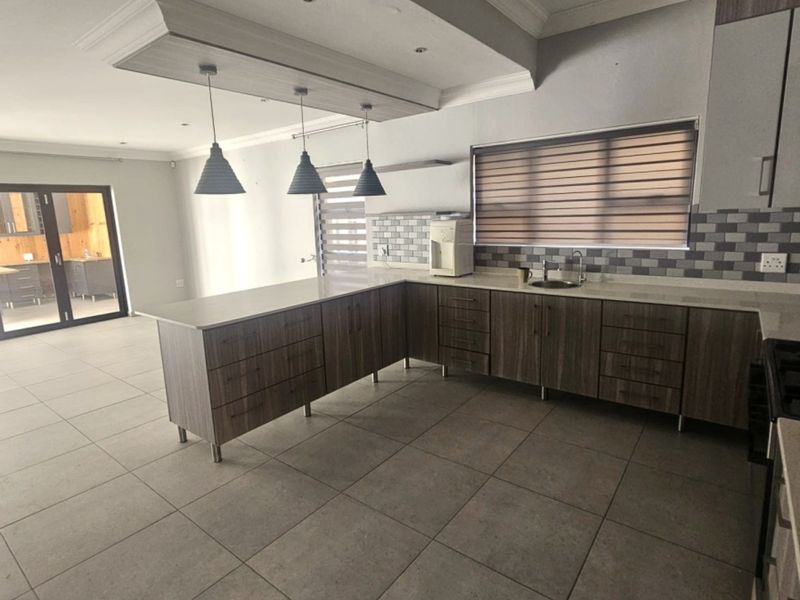 Spacious open-plan kitchen featuring modern wood-finish cabinetry, stone countertops, a central island, and large floor tiles, seamlessly connecting to the adjacent living area.