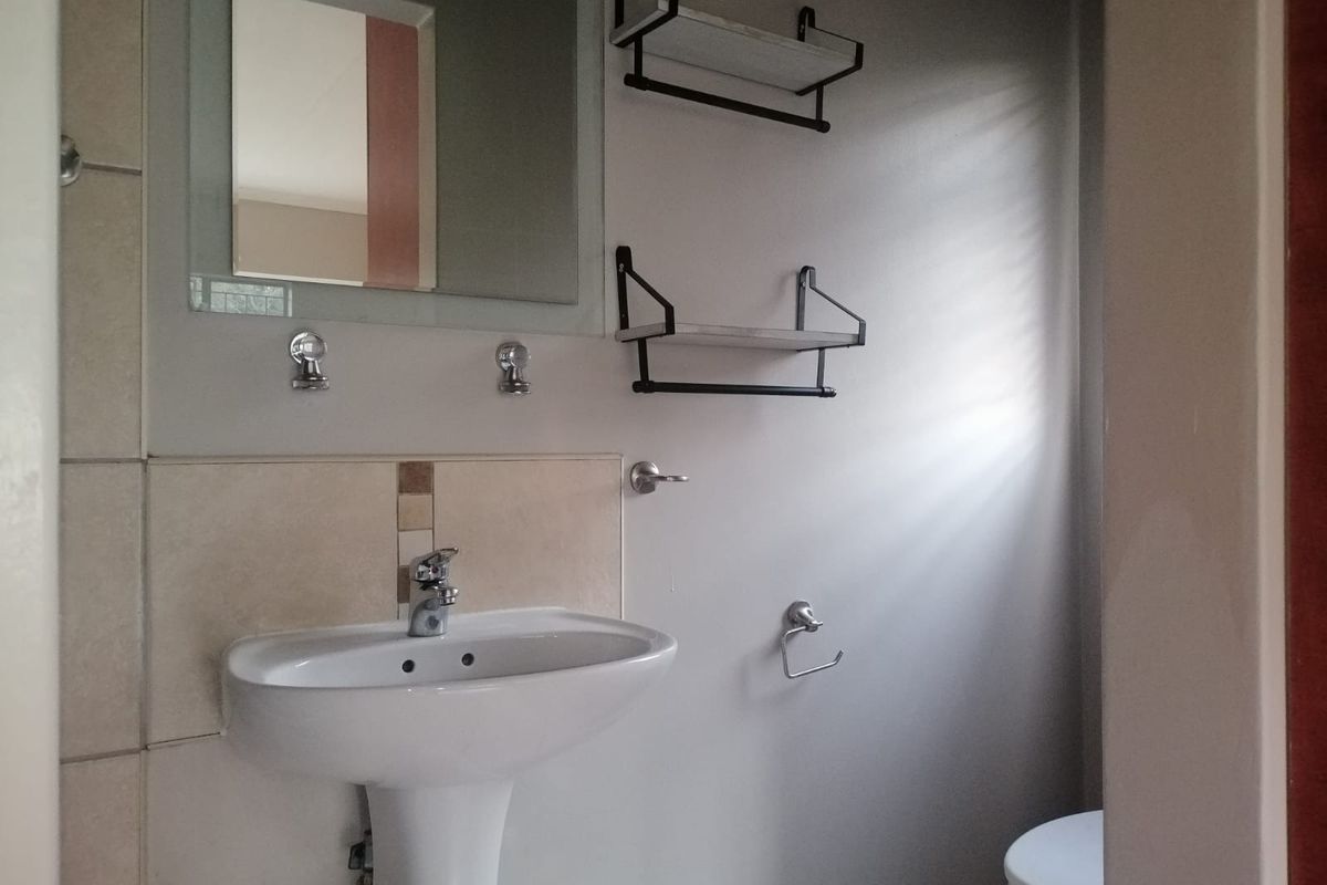 A clean and functional bathroom featuring a white pedestal basin, chrome fixtures, wall-mounted shelving, and neutral ceramic tiling.