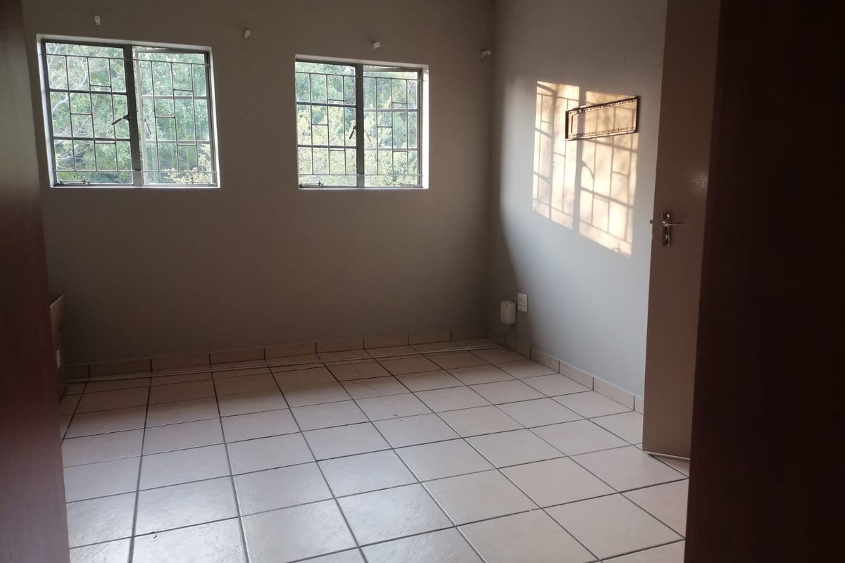 An empty bedroom featuring tiled flooring, security bars on the windows, and neutral wall finishes, offering a blank canvas for personalization.